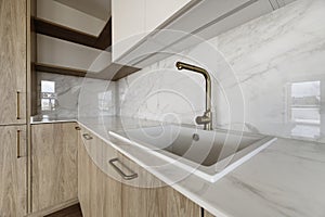 Corner of a newly installed modern kitchen with a white resin sink with a gold metal faucet on a quartz-like stone countertop and