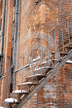 Corner of an old brick building with a metal staircase, snowball lies on rusty steps, background