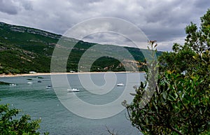 Corner with several boats in the sea, view to Praia do Creiro, with green mountain in the background of the Natural Park of Serra photo