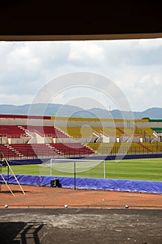 A corner of a soccer field with lush green grass, colorful spectator seats, and a backdrop of green hills