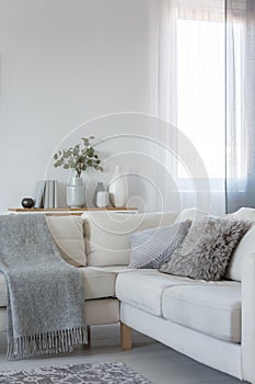 Corner sofa with pillows and blanket, copy space on empty white wall