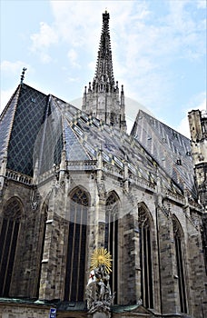 Corner of the Vienna Cathedral, with statues holding up a flag and a golden coat of arms with rays like the sun.