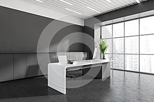 Corner view on dark grey office room interior with ceo table, desk with desktop computer, armchair, panoramic windows, concrete