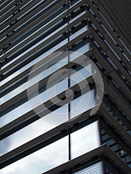 Corner view of a modern futuristic office building with blue sky and clouds reflected in the glass