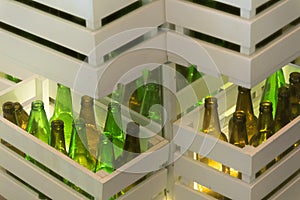 Corners of shelves made from white painted wood crates with transparent glass bottles inside. Retro style beer bottle rows.