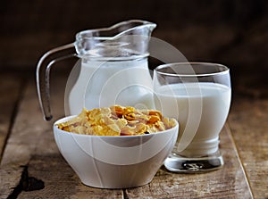 Cornflakes in bowl and glass of milk on wooden table