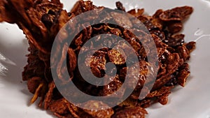 Cornflakes with chocolate flavor are pouring into a white plate in slowmo in macro