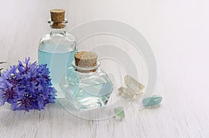 Cornflower flower and blue water or aromatherapy oil in glass bottle. Natural mineral crystals on white wooden table background