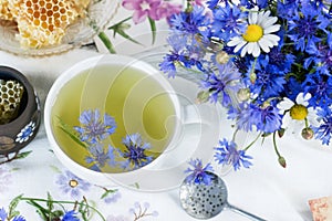Cornflower herbal tea in white cup on white crochet napkin intdoors, healthy cornflower drink with honey