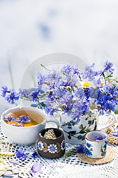 Cornflower herbal tea in white cup on white crochet napkin on wooden table outdoors