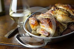 Cornish hens in an aluminum baking pan right out of the oven, shown with stemless glass of white wine and vintage fork.