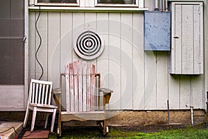 A corny backyard, with a dart target on a wooden wall where the paint flakes with wooden chairs