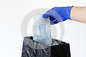 Corona virus or covid-19 protection concept. Male hand in latex glove throws in trashcan used medical mask against coronavirus