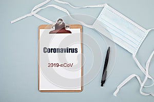 Coronavirus 2019-nCoV text on clipboard, disposable medical mask, personal protective equipment, syringe filled medicine or