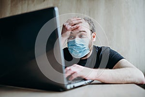 Coronavirus, an adult male with a beard works at a laptop. Protective respiratory mask.