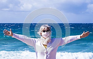 Coronavirus. Attractive senior woman with wind in her hair enjoying beauty of the sea, wearing a protective mask against