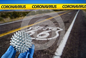 Coronavirus ball with US road with a Route 66 sign painted on it on the background