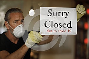 Coronavirus closed for business concept, male with medical mask puts sorry closed sign on window due to covid 19 pandemic