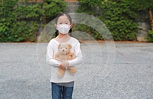 Coronavirus covid-19 and pollution protection concept. Asian little child girl hugging teddy bear doll with wearing mask to