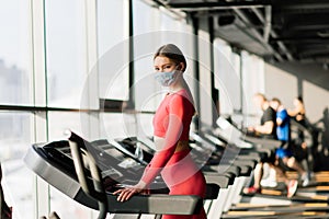 Coronavirus covid-19 prevention, fitness girl with a medical mask posing in gym. Fighting viruses