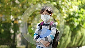 Coronavirus COVID-19 quarantine pandemic, portrait of a schoolboy wearing a protective mask outdoors in the open air