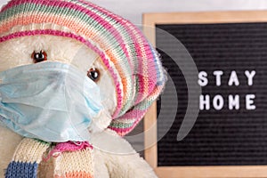 Coronavirus Covid-19 self isolation concept. Teddybear with medical mask against Letterboard with words stay home