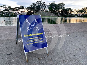 Coronavirus COVID-19 social distancing signboard warning people to stay six feet apart in front of lake