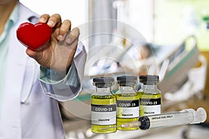 Coronavirus Covid-19 Vaccine in bottle and syringe for against virus with doctor holding red heart in hand on blur image