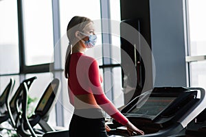 Coronavirus covid-19 prevention, fitness girl with a medical mask posing in gym. Fighting viruses