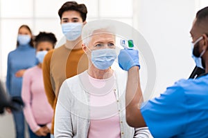 Worker Doing Temperature Screening Scanning Lady`s Forehead With Themometer Indoors photo