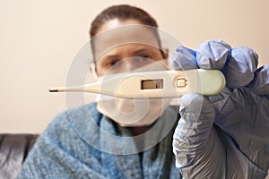 Coronavirus diagnosed patient wearing medical face mask in home isolation checking body temperature