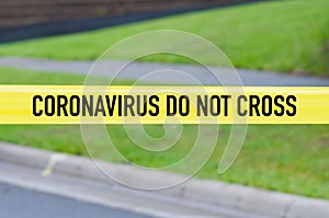 Coronavirus do not cross yellow warning tape with street and green yard in background