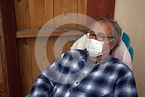 Coronavirus. Elderly gray-haired sick man with corona virus wearing mask protection recovering from the illness in home.