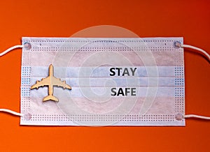 Coronavirus flight cancellations concept. Face mask and airplane toy on orange background. Words `stay safe`. Copy space