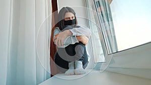 coronavirus. girl kid looks out window sad in a medical mask. stay at home. pandemic self-isolation coronavirus