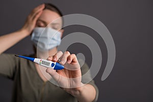 Coronavirus, a girl in a mask holds a temperature meter with a high temperature, on a gray background. Headlines for media, news.