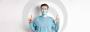 Coronavirus, health and quarantine concept. Handsome caucasian male model showing banner on top, pointing fingers up and