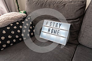 Coronavirus home lightbox sign with hashtag message  STAYHOME glowing on home sofa with cozy. COVID-19 text to promote self