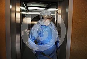 Coronavirus infection. Paramedic in protective mask and costume disinfecting elevator with sprayer