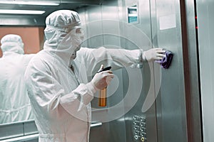 Coronavirus infection. Paramedic in protective mask and costume disinfecting an elevator with sprayer,