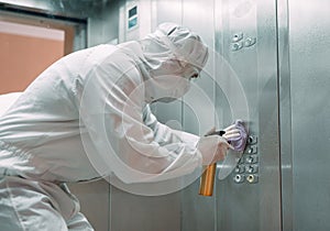 Coronavirus infection. Paramedic in protective mask and costume disinfecting an elevator with sprayer,