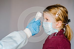 Coronavirus. Nurse or doctor checks girl`s body temperature using infrared forehead thermometer gun for virus symptom - epidemi