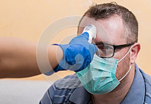 Coronavirus nurse wearing gloves and holding medical infrared forehead thermometer to check body temperature for virus symptoms