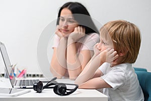 Coronavirus Outbreak. Lockdown and school closures. Mother helping her son studying online classes at home. COVID-19 pandemic