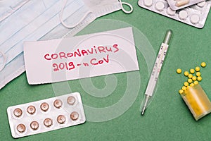 Coronavirus outbreak. Note with text 2019-nCoV, pills, respiratory masks and thermometer on a green background. The concept of a