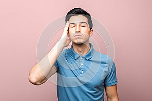 Coronavirus pandemic only bad news. exhausted adult man in blue shirt with headache holding his hand over his temple