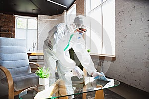 Coronavirus Pandemic. A disinfector in a protective suit and mask sprays disinfectants in the house or office