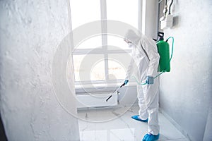 Coronavirus Pandemic. A disinfector in a protective suit and mask sprays disinfectants in house. Protection against COVID-19