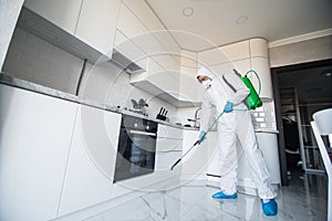 Coronavirus Pandemic. A disinfector in a protective suit and mask sprays disinfectants in house. Protection against COVID-19 photo