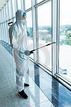 Coronavirus Pandemic. A disinfector in a protective suit and mask sprays disinfectants in office. Protection agsinst COVID-19